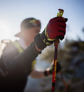 A hand grips a red trail running pole in backlight.