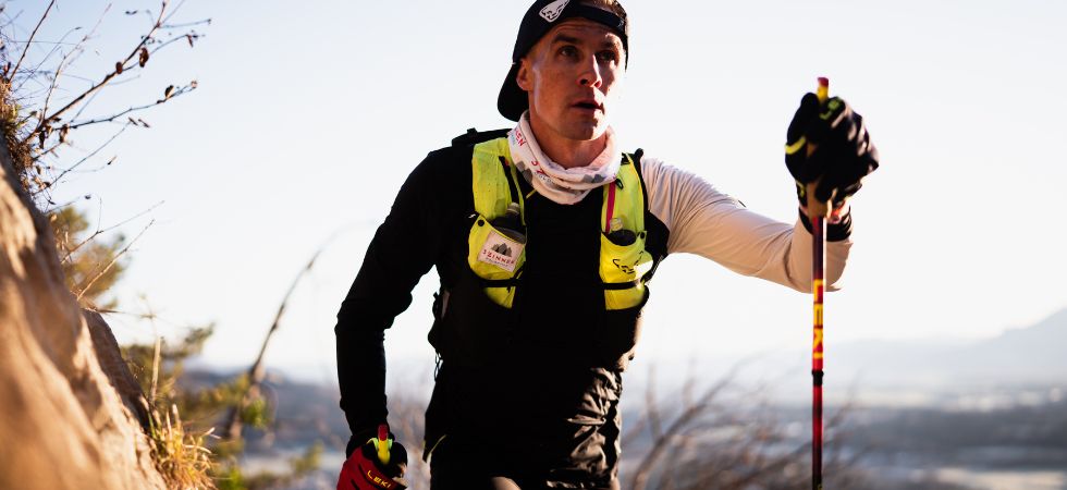 A trail runner climbs a sunny slope with poles.
