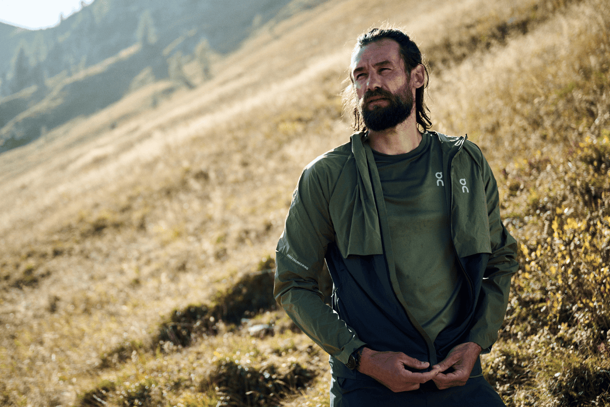 A man takes a break while running. He zips up his jacket. 