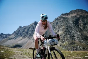 Eine Radfahrerin fährt mit Gepäck am Bike durch eine alpine Berglandschaft.
