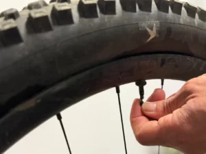 Eine Hand öffnet das Ventil am Fahrradreifen zur Kontrolle des Reifendrucks.