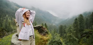Wanderin mit Rucksack genießt die Aussicht in einer nebligen Berglandschaft.