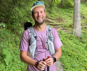 Christian Pacher steht lächelnd mit Stöcken auf einem Waldweg.