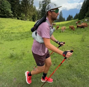 Ein Läufer trainiert Trailrunning Lauftechnik mit Stöcken auf einer Almwiese.