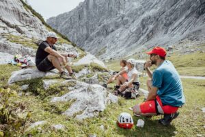 Climbing group taking a break in a rocky mountain landscape with helmets and outdoor clothing.