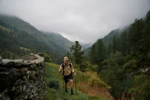 Hiker with trekking poles on a mountain trail in a misty valley.