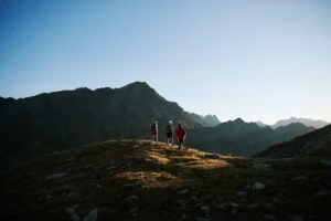 Drei Wanderer unterwegs bei Sonnenaufgang auf einem alpinen Höhenweg.