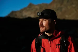 Wanderer mit Stirnlampe und roter Jacke bei einer Sonnenaufgangswanderung in den Bergen.